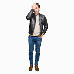 Middle age handsome man wearing black leather jacket surprised with hand on head for mistake, remember error. Forgot, bad memory concept.