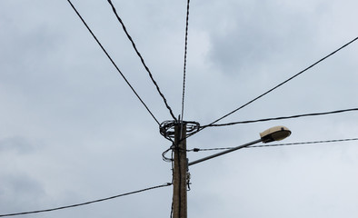 Electric pole with many cables of electric lines and a street lamp.
