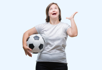Young adult woman with down syndrome holding soccer football ball over isolated background very happy and excited, winner expression celebrating victory screaming with big smile and raised hands