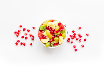Fruit diet concept. Fruit salad with apple, kiwi and pomegranate in bowl on white background top view copy space