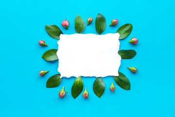 Floral mockup. Flowers, petals, leaves around white paper on blue background top view frame