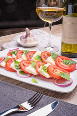 Caprese salad on a blue plate with an ornament on a light table in a restaurant.