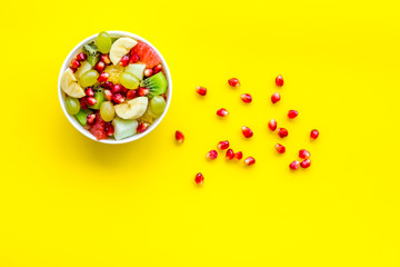 Light healthy breakfast or appetizer. Fruit salad with apple, kiwi and pomegranate in bowl on yellow background top view copy space