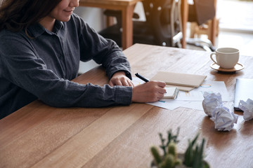 Closeup image of an asian businesswoman working and writing down on a white blank notebook with screwed up papers and laptop on table in office