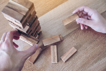 Closeup image of two people's hand holding and playing Tumble tower wooden block game
