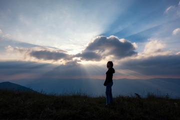 A woman standing and watching sunset with mountains view in the evening