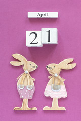 Wooden cubes calendar April 21 and pair of wooden easter bunnies on purple paper background....