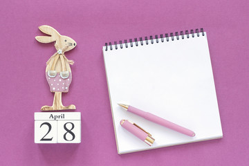 Calendar April 28, wooden easter bunny, white notepad on purple paper background. Concept Christian Easter Mockup Template for lettering, text or your design Creative Top View.