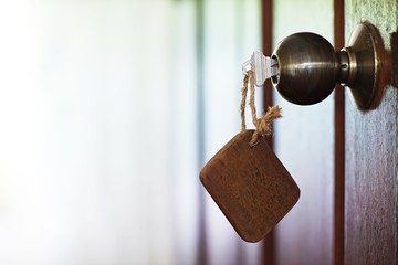 Home key with wooden blank house keychain in keyhole, property concept