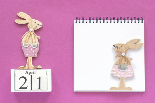 Calendar April 21 and pair of wooden easter bunnies, white notepad on purple paper background. Concept Catholic Easter Mockup Template for lettering, text or your design Creative Top View.