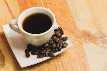 taza de café blanca en un plato blanco con granos de café en una mesa de madera