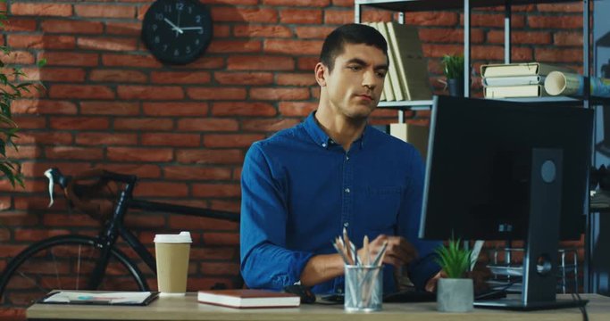 Portrait shot of the Caucasian attractive young man working on the laptop computer at the working place and thinking hard.