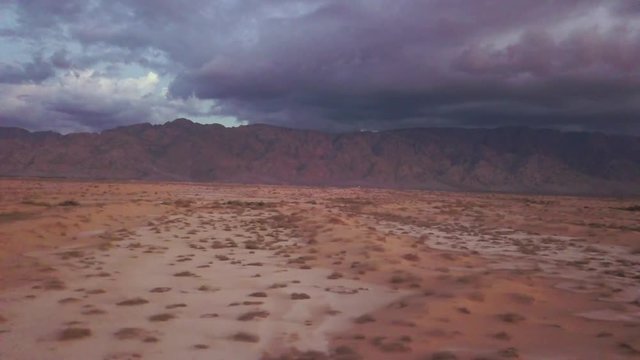 Israel Aerial Drone Of Middle Eastern Camel Owners In Desert Convoy Tourism. Flying View Edom Mountains Arava Rocky Desert with Sand sandy desert and clouds. kibbutz in southern Israel