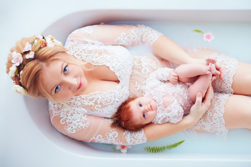 young happy mother with newborn baby girl, daughter in floral milk bath, family look outfit