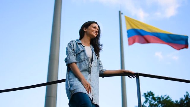 Beautiful young girl in front of Colombian flag in the wind, Smiling happy tourist posing in front of Colombian flag