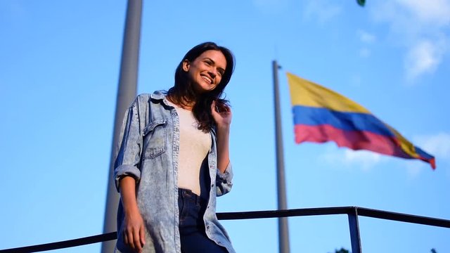 Proud smiling young woman standing in front of the Colombian national flag, Beautiful smile girl posing in front of the Colombia flag on the wind, perfect blue sky