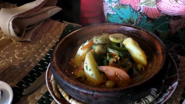 Woman at the table in Moroccan cafe is waiting for hot steaming vegetarian tajine or tagine cooling off