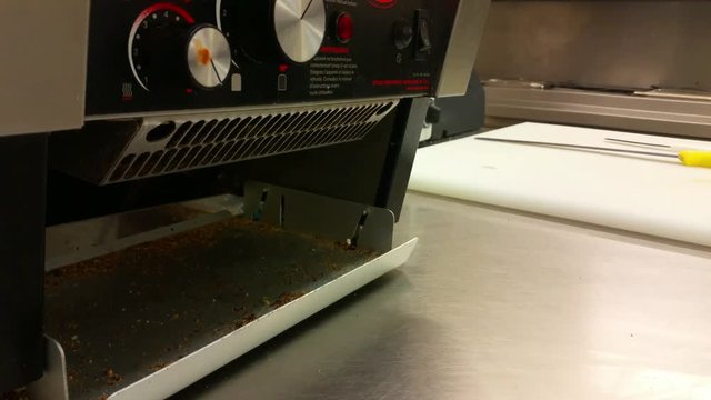 Low angle sliding shot across stainless steel catering kitchen machines with bread knife on chopping board.