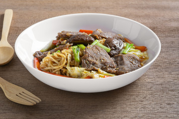 hot and spicy stir fried instant noodle with beef and vegetable in a ceramic plate on wooden table. asian homemade style food concept.