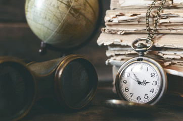 Travel or adventure concept background. Pocket watch, binoculars, globe and stack of books on the adventurer table.