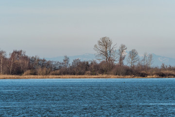 river reflecting the blue sky with small island with trees and mountain range in the background on a hazy day