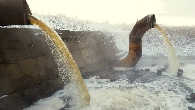 Wastewater from two large rusty pipes merge into the river in clouds of steam