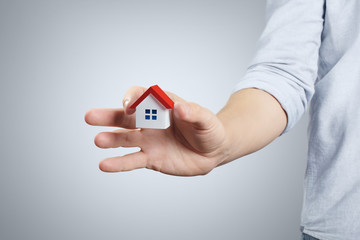 Hand holding a small red roofed house on gray background