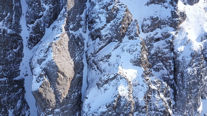 Fototapeta na wymiar Huge rocks covered with snow. Ledges from the snowy mountains. Cliffs and large rocks. Dangerous terrain. Drone view from the top and side. The sun's rays on the Shadow of the mountains.