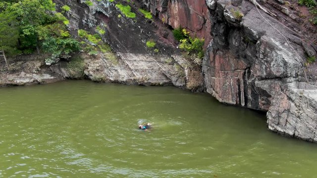 Adult male emerging on water surface after jumping from cliff, razor sharp rocks in background, outdoor extreme sports concept