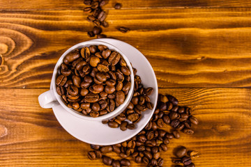 White cup filled with coffee beans on wooden table. Top view