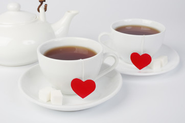 Tea for two. Two white cups of tea with labels in the form of red hearts. On a white background