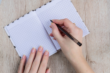 young woman hands hold opened notebook pages with black pen on  wooden table