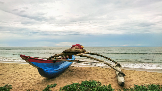 Traditional blue fishing boat on an empty and calm beach of Sri Lanka.