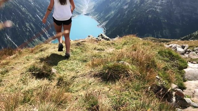 Slow motion shot of girl running down grassy mountain top overlooking the beautiful and famous Lake Schlegeis, Austria