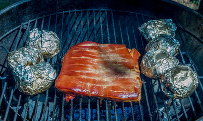 Red meat and potatoes wrapped in foil slowly cooking in an outdoor kettle oven image with copy...