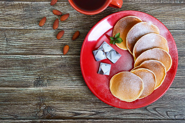Tasty pancakes with powdered sugar on a red plate on a wooden table. Top view. Holiday card. Festive dessert on the theme of love.