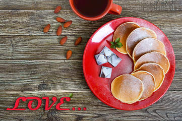 Tasty pancakes with powdered sugar on a red plate on a wooden table. The inscription 