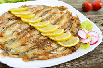Baked capelin on a white plate on a wooden table. A dish of small fish