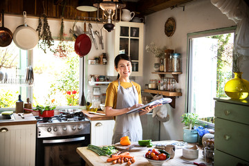 Happy woman reading a cookbook in the kitchen