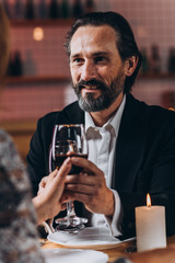 Middle-aged man smiles happily and raises a glass of red wine with a woman