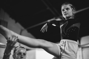 Coach training young gymnast to balance on a balance beam