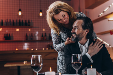 Woman stands behind a man with her hand on his shoulder  and hand touches cheek