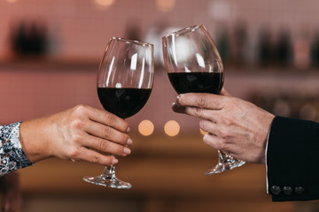 Closeup of glasses with red wine in the hands of a man and a woman in the center of the frame