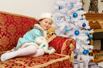 Obraz na płótnie Canvas Little girl in the snow maiden costume with a teddy bear near th