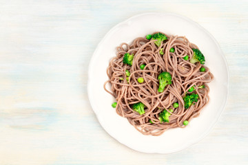A plate of cooked soba, buckwheat noodles with healthy green vegetables, shot from the top with copy space