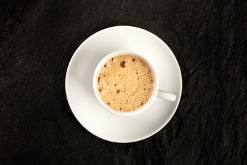 A photo of a cup of coffee with foam, shot from the top on a black background with a place for text