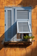 Blue shuttered window with a small plant against an orange wall in  a house in rural France