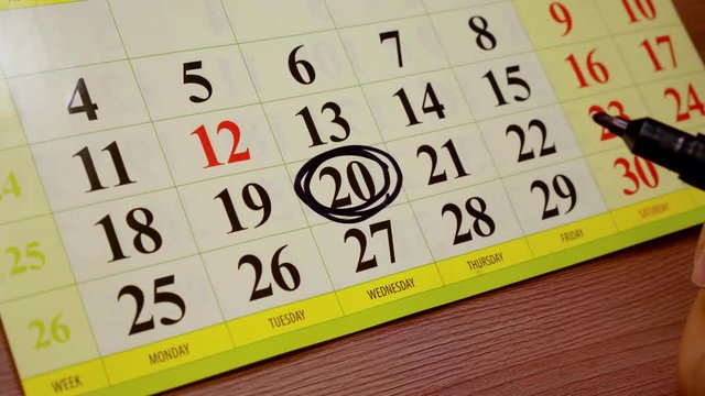 human is outlining twentieth day in calendar using black marker, close-up view