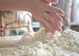 A woman in a colored apron rubs her fingers through the dough on the table.