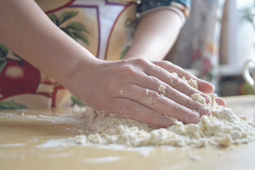 Obraz na płótnie Canvas A woman in a colored apron kneads dough on the table.